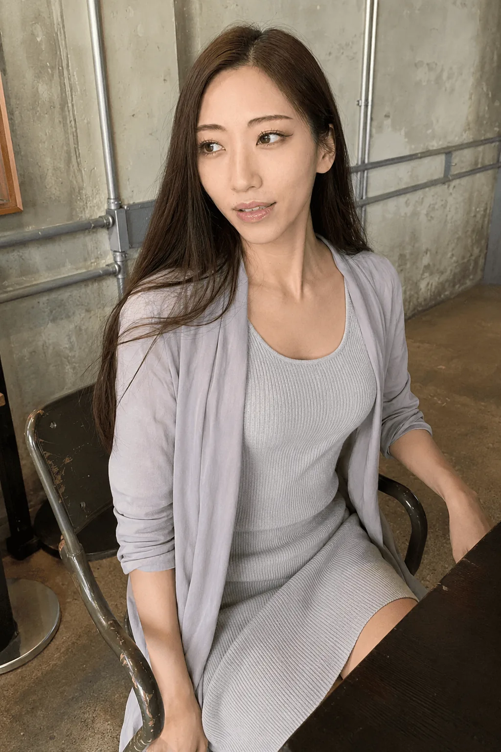 室内の椅子に淡いグレーのワンピースとカーディガン姿で座り横を見る人物