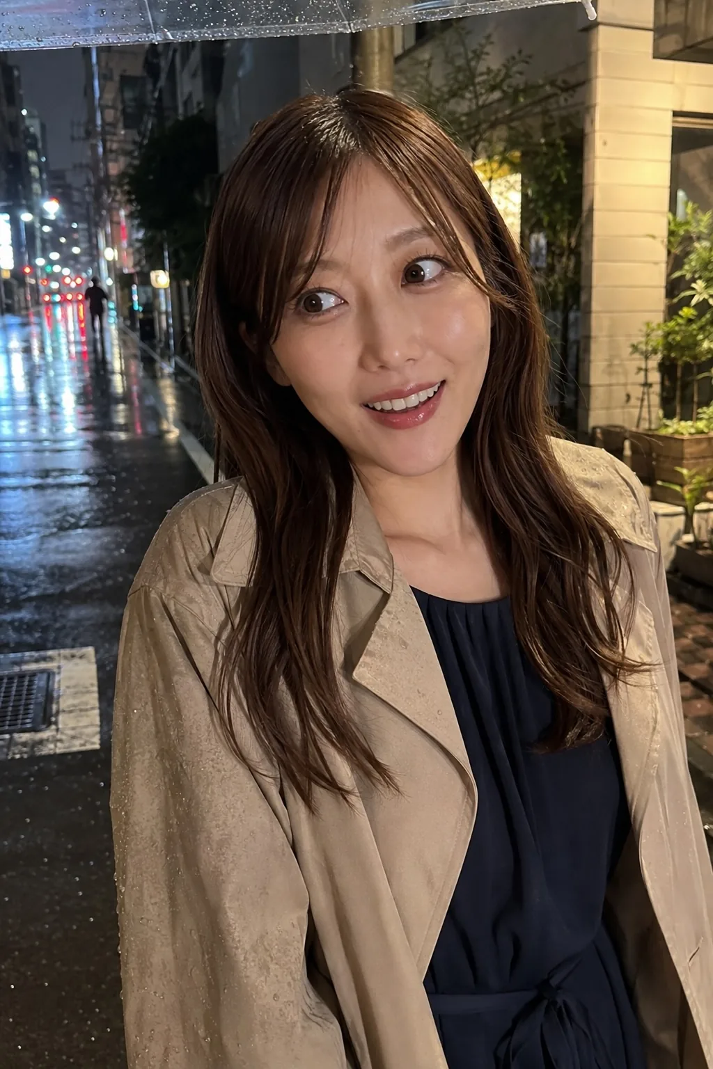 雨の夜の街路で紺のワンピースとベージュのジャケットを着て口を開けて笑う人物