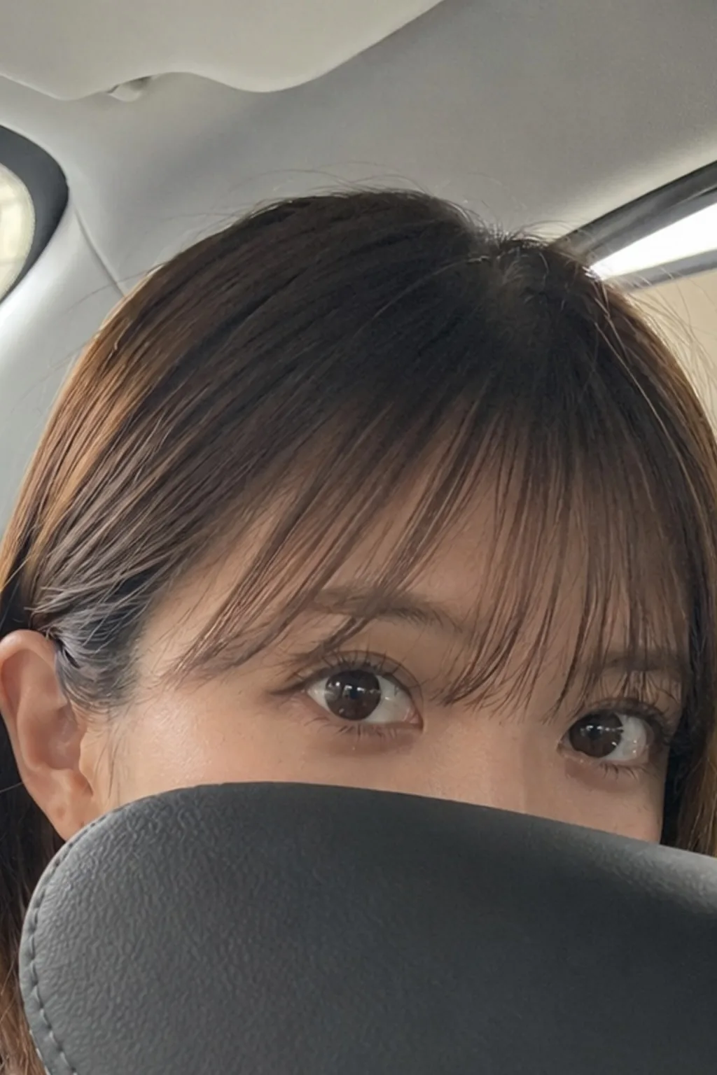 車内の座席で背もたれの上から目元をのぞかせる人物